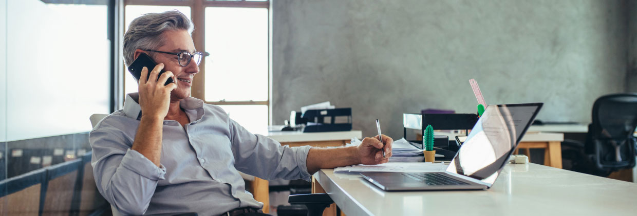 A business man sitting at a desk, engaged in a phone conversation.