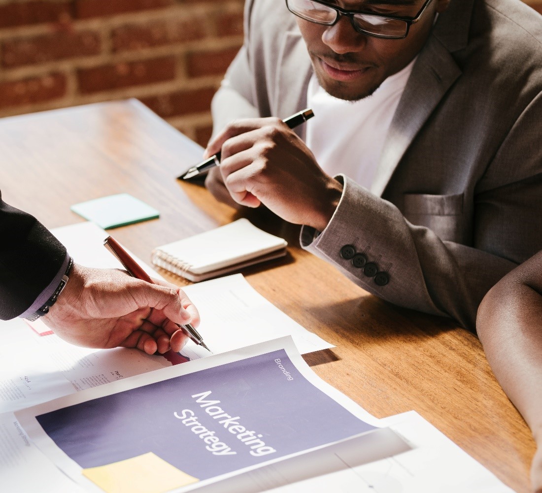 people holding pens in a business meeting examining a marketing strategy document