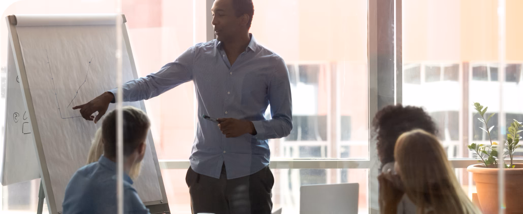 A man confidently presenting to a group of attentive individuals, engaging them with his informative presentation.